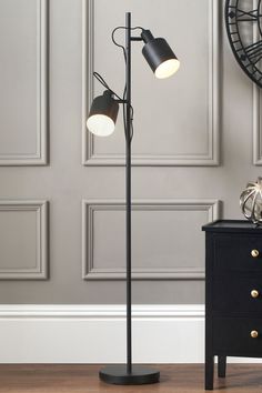 a black floor lamp with two lamps on each side and a clock in the background