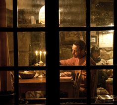 a man sitting at a table in front of a window with candles on the windowsill