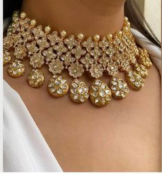 a woman wearing a gold necklace with lots of stones and pearls on the neck,