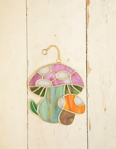 a colorful stained glass ornament hanging on a white wooden wall with an orange fish