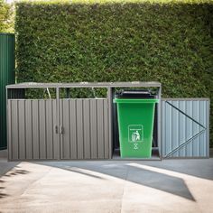 a green trash can sitting next to a metal fence with a garbage bin in front of it