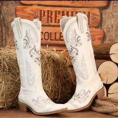 a pair of white cowboy boots sitting on top of hay next to stacks of logs