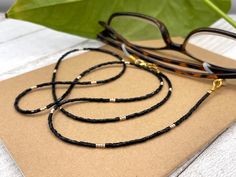 Elegant and bohemian eye glasses necklace chain in black and gold tones made of crystal bugle seed beads and tiny gold plated crystal seed beads. Paired with delicate gold plated crystal seed beads , this handmade eyeglass chain will definitely create a unique look. This eyeglass lanyard is made on strong quality beading wire with gold plated wire guardians that protect the quality white eyeglass holder grips. The necklace is ended with spring clasps that hold the eyeglass grips and they can be Glasses Necklace, Glasses Lanyard, Beaded Sunglasses, Eyeglasses Chain, Sunglasses Necklace, Grandma Necklace, Eyeglass Chain, Eyeglass Holder, Beading Wire