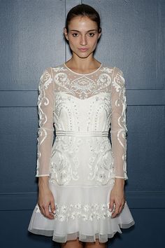 a woman standing in front of a blue wall wearing a white dress with sheer sleeves