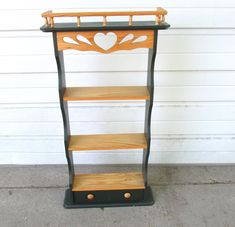 a three tiered shelf with hearts painted on the top and bottom, sitting in front of a garage door