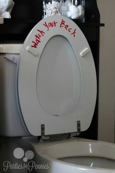 a white toilet with red writing on the lid next to a trash can and shelf