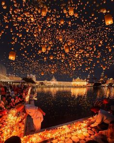 many people are flying lanterns over the water