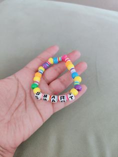 a person's hand holding a colorful bracelet with the word smart written on it