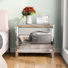 a mirrored nightstand with flowers and pictures on it in the corner of a room next to a bed