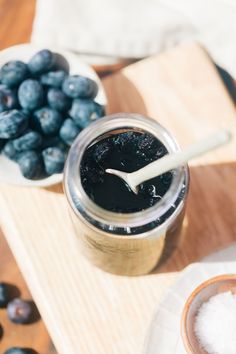 a jar of blueberry jam next to a bowl of fresh blueberries on a cutting board