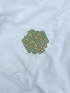 there is a baby cole sign on top of the bed sheet that's white with gold lettering