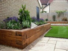 a wooden planter filled with lots of plants next to a brick wall and green grass