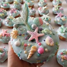 a hand holding a doughnut covered in blue frosting and sea life decorations on top of it