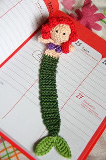 a crocheted mermaid doll hanging from a clipboard on top of a notepad