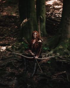 a woman with red hair and makeup holding two arrows in the middle of a forest