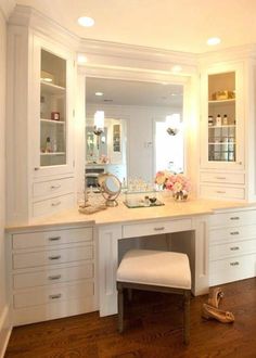 a white vanity with drawers and stool in a room that has hardwood floors, built - in shelving, and large mirror on the wall