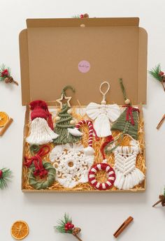 an open box filled with assorted christmas ornaments on top of a white table next to orange slices and cinnamon sticks