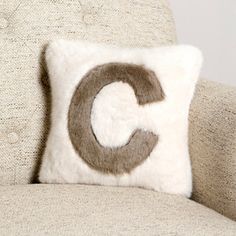 a white and brown pillow sitting on top of a couch next to a beige chair