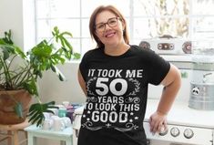 a woman standing in a kitchen wearing a t - shirt that says it took me 50 years to look this good