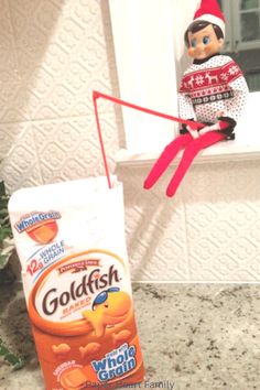 an elf is sitting on the window sill next to a bag of goldfish cereal