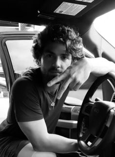 a man sitting in the driver's seat of a car with his hand on the steering wheel