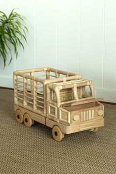 a toy truck made out of bamboo sitting on the floor next to a potted plant