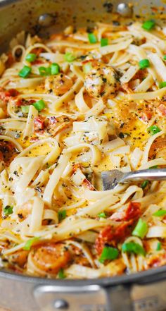 a pan filled with pasta and vegetables on top of a wooden table next to a fork