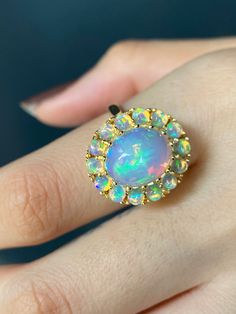 RING DETAILS: ✪Design: Gold ring ✪Gemstone: Opal ✪Gemstone shape: Cabochon oval ✪Gemstone size: Center stone: 12x10mm Oval, side stones: 3mm round ✪Setting type: Cluster ✪Metal type: 14k solid yellow gold (also available in white and rose gold, please select at checkout) ✪Total ring weight: 7 grams ✪Metal finish: Smooth shiny Choose your ring size from drop down menu and if you need any other preferred ring size please contact us. QUALITY OF MATERIALS: Metal: Most of our jewelry at JewelryMansio Fine Jewelry Opal Ring With Halo In 14k Gold, 14k Gold Opal Ring With Halo, 14k Gold Opal Halo Ring, 14k Gold Round Opal Halo Ring, 14k Gold Halo Opal Ring, 14k Gold Multi-stone Round Jewelry, 14k Gold Multi-stone Round Gemstones, Oval Multi-stone Cluster Ring Fine Jewelry, Yellow Gold Gemstones With Halo Setting