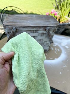 a hand holding a green micro towel over a table with a basket in the background