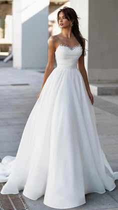 a woman in a white wedding dress standing on the sidewalk