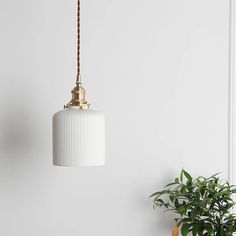 a white lamp hanging from a ceiling next to a potted plant on a table