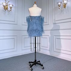 a mannequin wearing a blue feathered dress on a stand in front of wall sconces