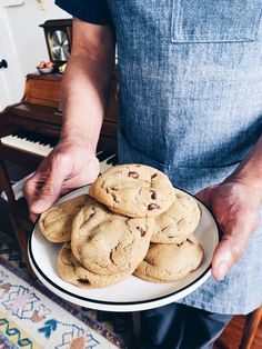 a person holding a plate with chocolate chip cookies on it and a piano in the background