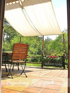 a wooden chair sitting on top of a patio under a white awning over a table