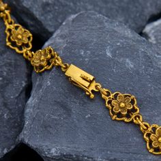 a gold bracelet with flowers on it is sitting on some rocks and has a lock in the middle