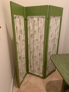 a green room divider sitting next to a wooden table in a corner with curtains on it