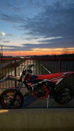 a red and black motorcycle parked on the side of a road at dusk with a full moon in the background