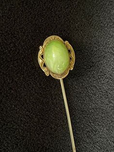 a green flower shaped brooch sitting on top of a black carpeted floor next to a metal spoon