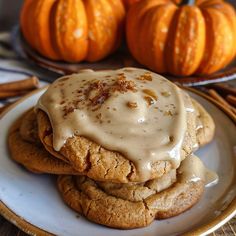 two cookies covered in icing on top of a white plate next to pumpkins