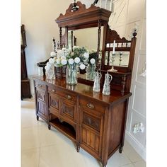 a wooden dresser with vases and flowers on it in front of a large mirror