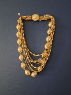 "Absolutely stunning large faux pearl and gold tone statement necklace.  Multi strand beaded necklace. The gold metal and faux pearls are vibrant and shiny.  Clear resin/plastic beads, plain gold chains and faux pearl beads adorn this gorgeous necklace.  Clasp is in great condition and closes/opens easily.  A great necklace to add to many different style outfits! Modern twist on your traditional pearl necklaces. Clean and ready to wear! Measurements are approximate: longest chain strand-10.5\" * Gold Beaded Metal Pearl Necklace, Gold Multi-strand Pearl Chain Necklace, Gold Pearl Beaded Necklaces With Chain, Gold Pearl Costume Jewelry Necklace, Gold Multi-strand Pearl Necklace For Party, Vintage Pearl Necklace With Chain For Parties, Vintage Gold Necklaces With Pearl Chain, Vintage Gold Pearl Necklace With Round Beads, Gold Multi-strand Pearl Necklaces