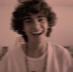 a blurry photo of a young man with curly hair smiling at the camera while wearing a white t - shirt