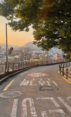 an empty street with graffiti painted on the road and trees in the background at sunset