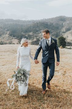 a bride and groom holding hands walking through a field