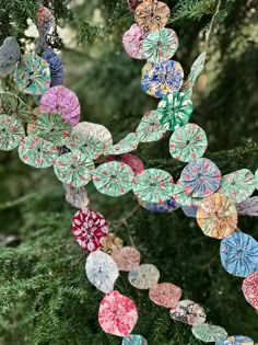 an ornament hanging from a tree decorated with colorful paper flowers and leaves in the shape of hearts