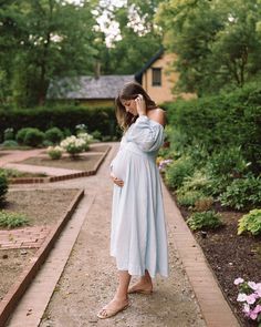 a pregnant woman in a white dress is talking on her cell phone while standing outside