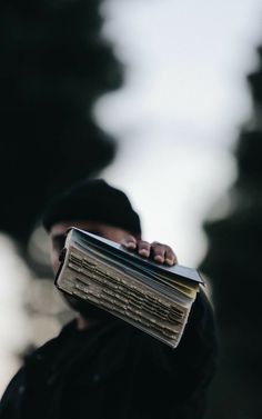 a man holding an open book in his hand while wearing a black hat and jacket