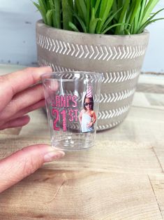 a person holding up a shot glass with an image of a woman's 21st birthday on it