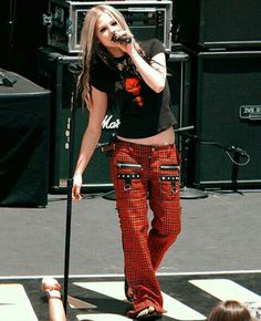 a woman standing on top of a stage holding a microphone in her hand and wearing plaid pants