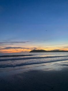 the sun is setting at the beach with waves coming in to shore and an island in the distance